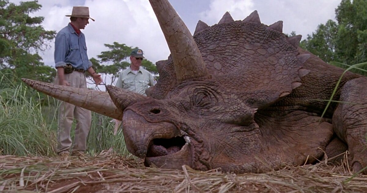 Sick triceratops lying on the ground with Grant and the vet Harding examining it