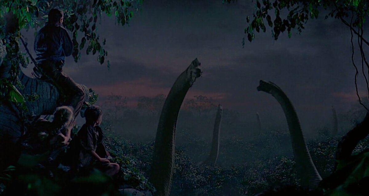Long-necked dinosaurs silhouetted against a sunset over the park